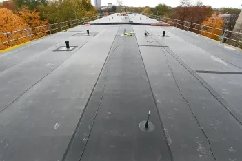 Pohled na dokončenou plochou střechu s EPDM fólií, svařenými spoji pásů a prostupy, v pozadí podzimní stromy.